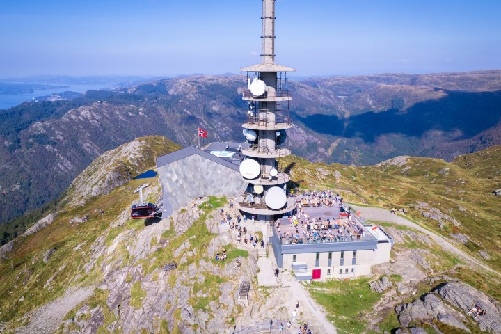 Mountain peak with communication tower, scenic views, and a small gathering of people.