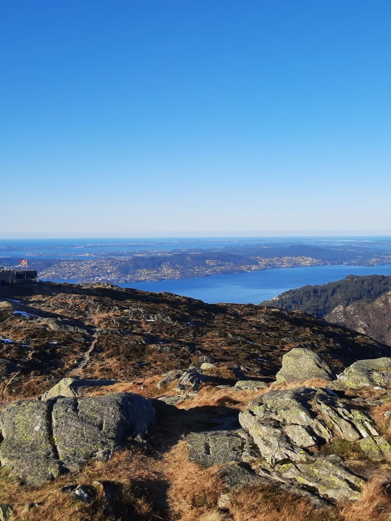 Rocky hilltop with distant view of sea and islands under clear blue sky.