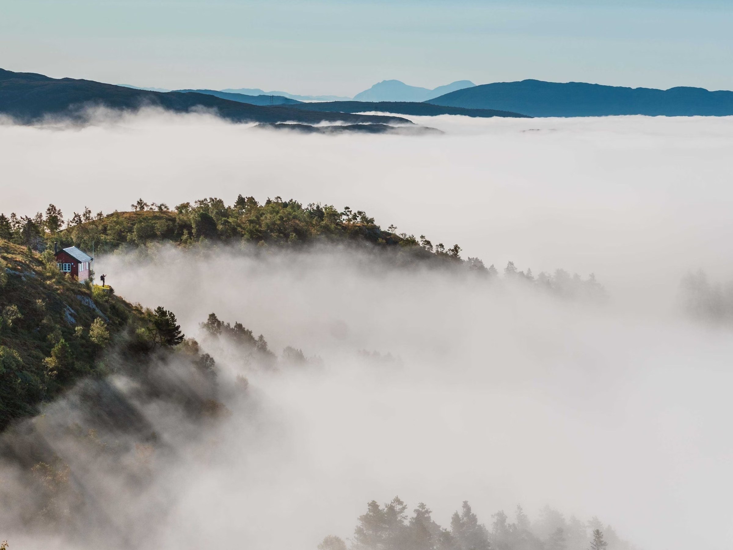 Foggy mountain landscape with distant peaks and a house on a hill.